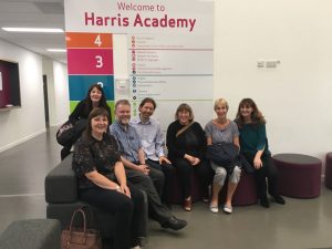 Seven people are sitting in the foyer of the newly built Harris Academy on a visit to their school library. Behind them is a sign which states Welcome to Harris Academy.