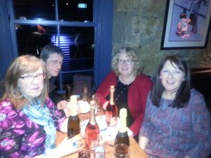 The winning team at the CILIPS Tayside Pub Quiz. Four people are sitting around their table looking at the camera, they have bottles of wine as their prize on the table in front of them.