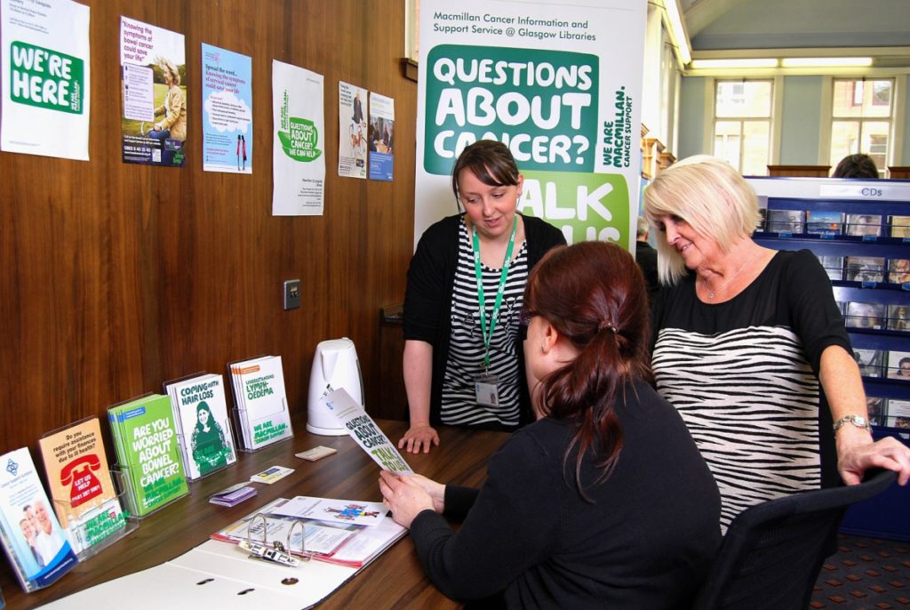 three women look at leaflets beneath a sign for Macmillan Cancer Support