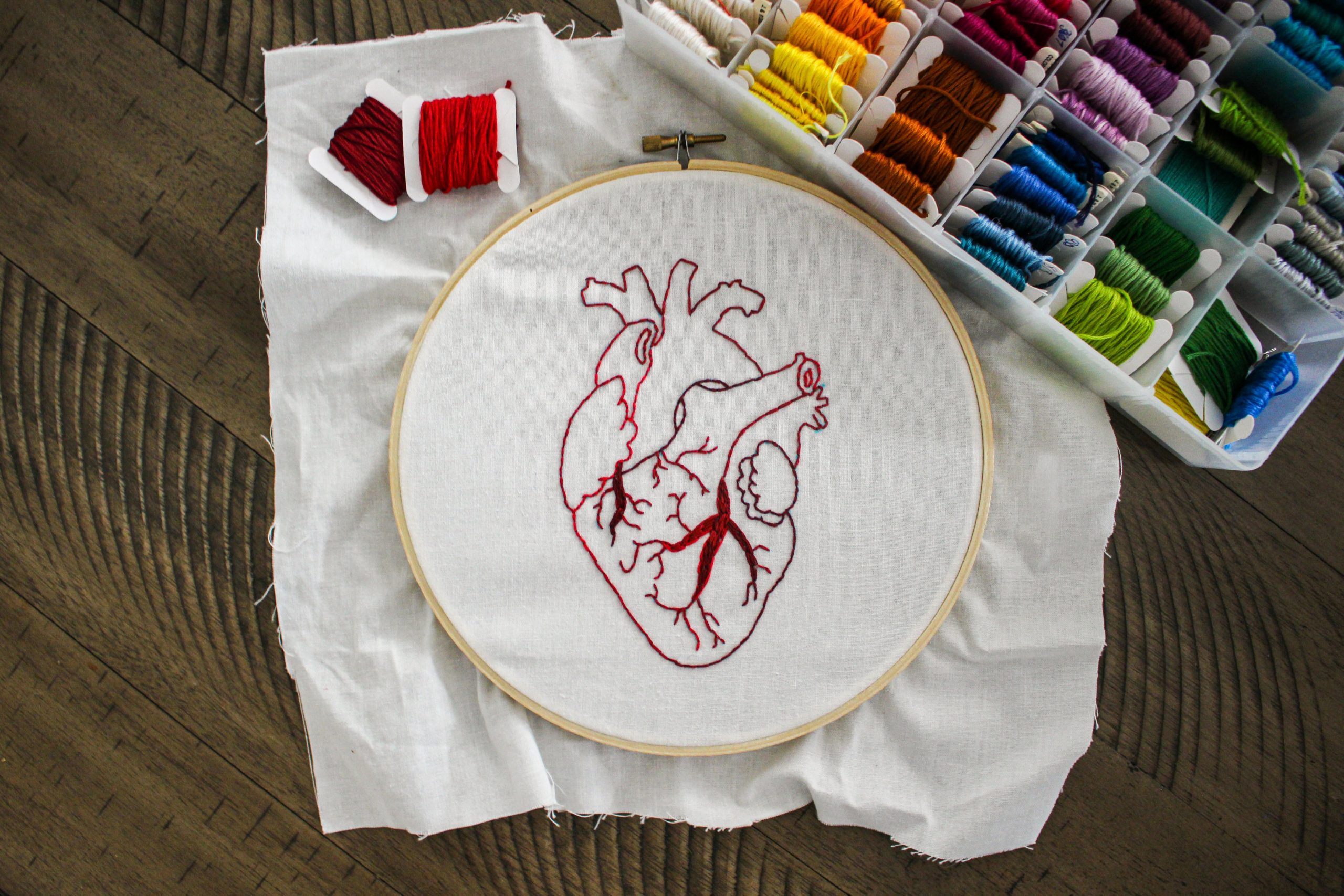 a heart sewn from red and burgundy thread, with a box of multicoloured threads beside it