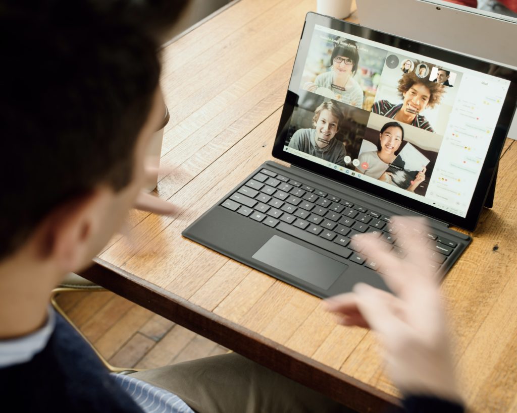 A man participating in a webinar on his laptop, with four people's smiling faces visible on screen.