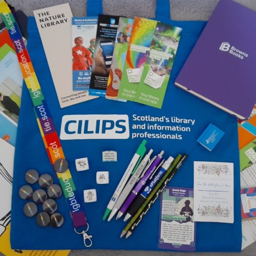 A flatlay photograph showing a delegate's conference bag with pencils, pens, badges, bookmarks, cards and more from our conference exhibitors.