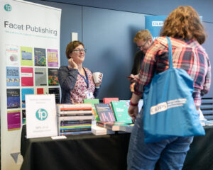 Exhibitors and a delegate browsing the Facet Publishing stand at the 2022 CILIPS Annual Conference.
