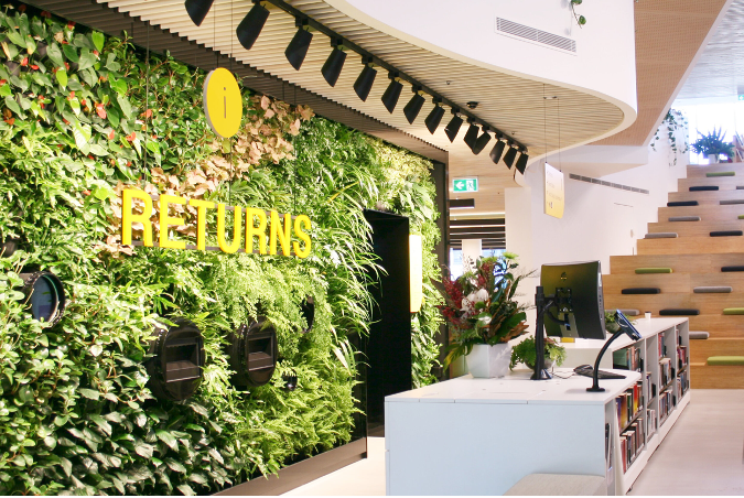 Green wall of plants behind wooden desk with yellow text that says returns.