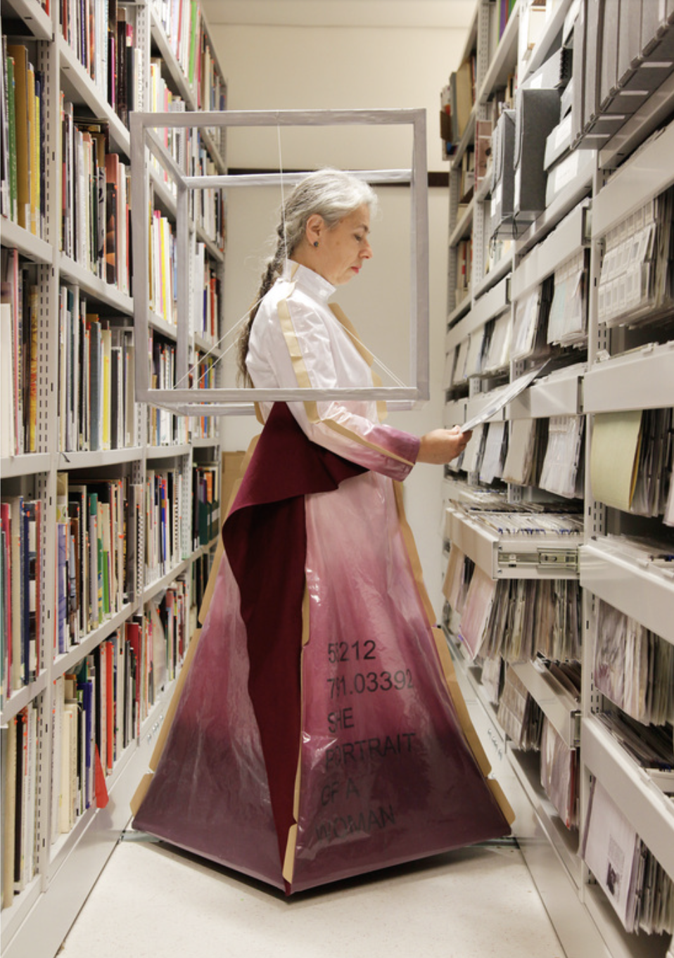 Image of Althea Greenan wearing a period costume looking at a book between the stacks. 