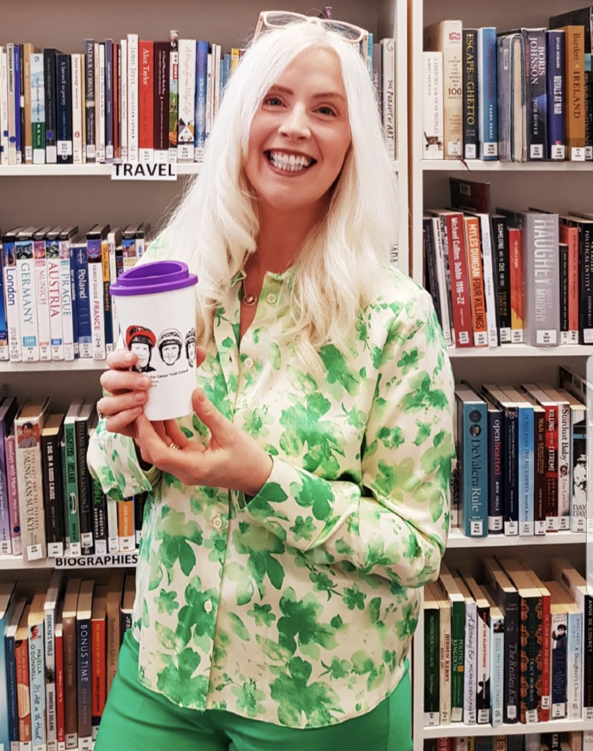Photograph of blog author Gillian holding a reusable cup in front of a bookshelf in the library. 