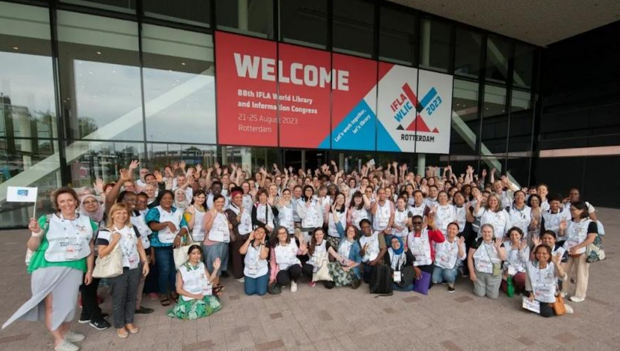 Volunteers in white tabards beneath a Welcome sign at the IFLA Congress in Rotterdam, 2023.